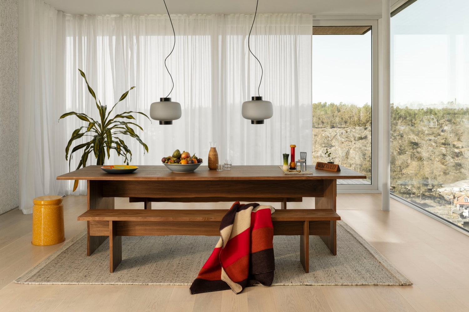 A lifestyle image of a dining scene featuring Bookmatch Table + Benches Set, Dusk Lamp Large, Dune Rug, Block Throw, Offcut Plate, and Last Stool.