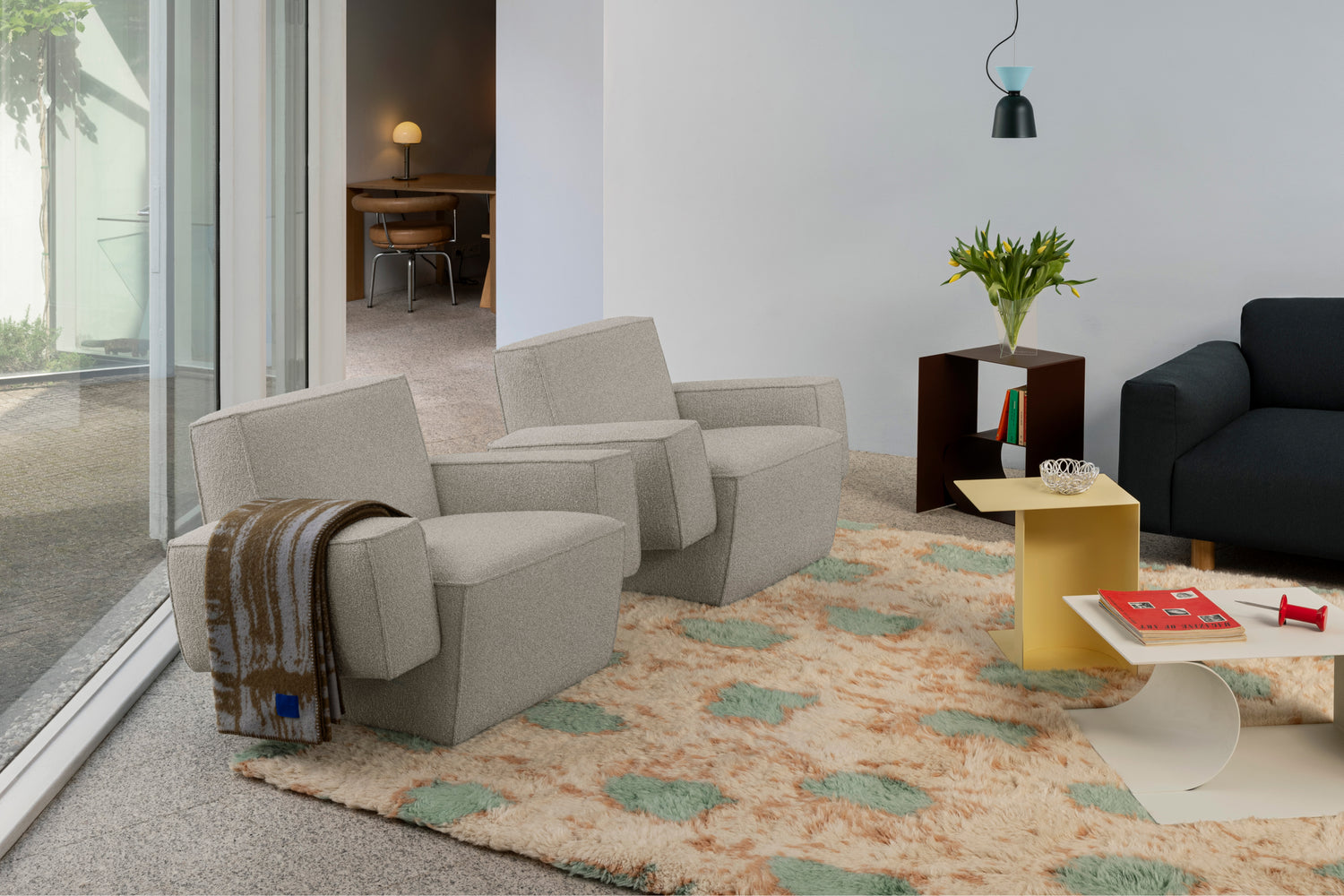 A lifestyle image of living room scene featuring Hunk Lounge Chair with Armrests, Glitch Throw, Monster Rug, Glyph Side Tables, and Alphabeta Pendant Light.