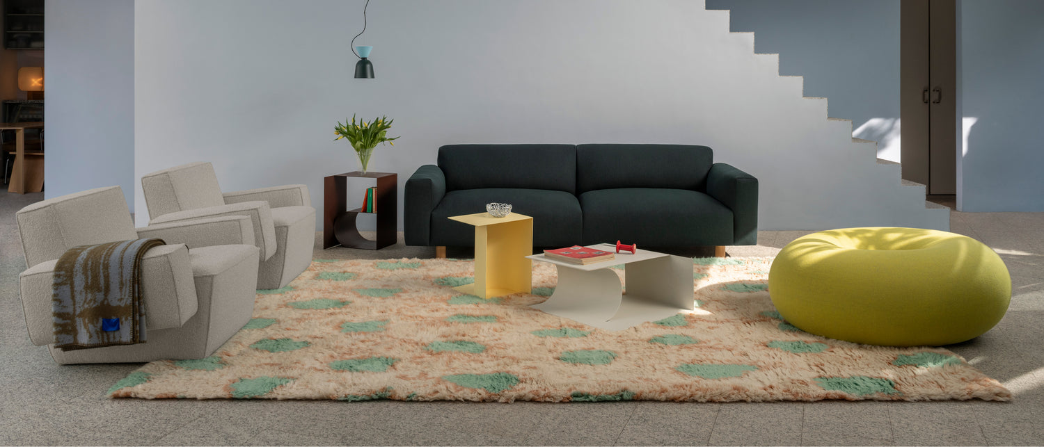 A lifestyle image of a living room scene featuring Hunk Lounge Chair with Armrests, Glitch Throw, Monster Rug, Alphabeta Pendant Light, Glyph Side Tables, Boa Pouf, and Koti 3-seater Sofa.