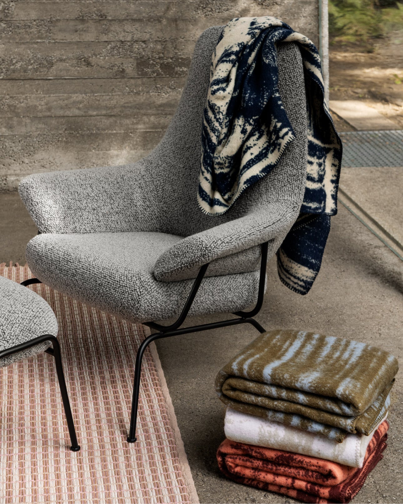 Hai Lounge Chair + Ottoman in Pebble with 4 Glitch Throws in the shades Coral / Rust Red, Sand / Off-White, Powder Blue / Olive Green and Pale Lemon / Navy Blue with a Rope Rug in Rose Quartz.