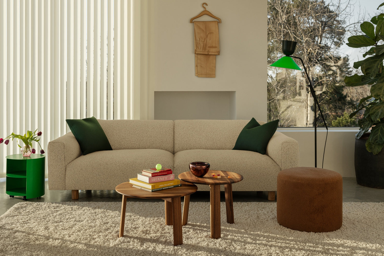 A living room scene featuring a Pure Green Hide Side Table, Alle Coffee Tables (set of 2) in Walnut, A Brown Bon Pouf Round, an Alphabeta Floor Lamp, and a Koti Sofa in the shade Eggshell.