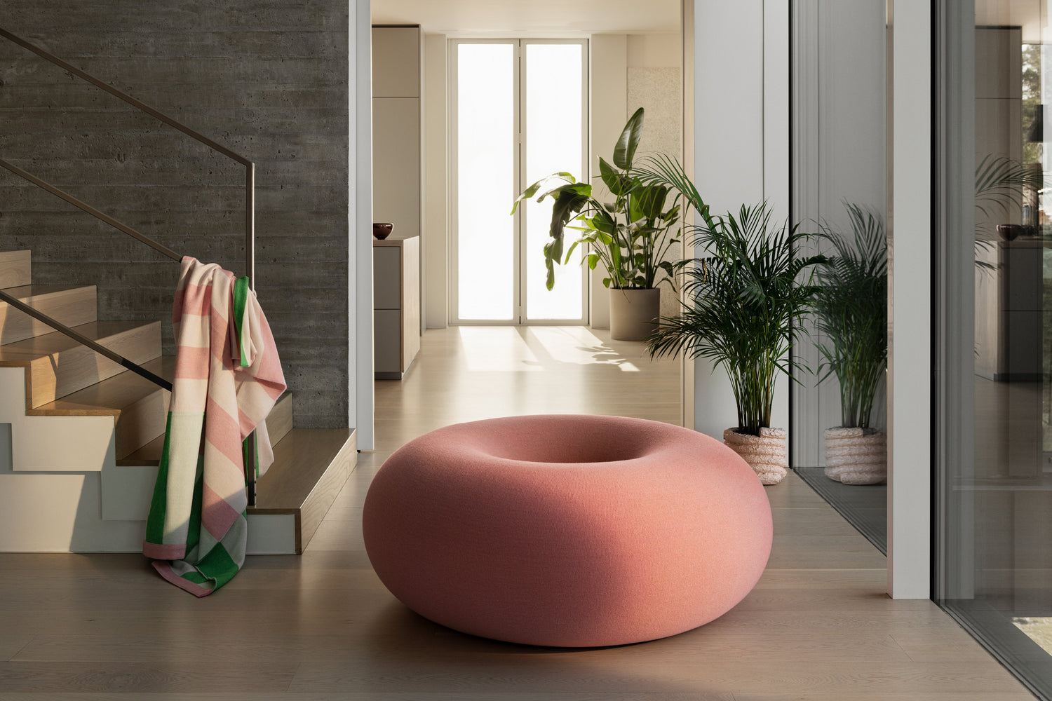 Boa Pouf in Cotton Candy featured in a hallway with a staircase on the side with a Stripe Throw in Pink / Green draped over the handrail.