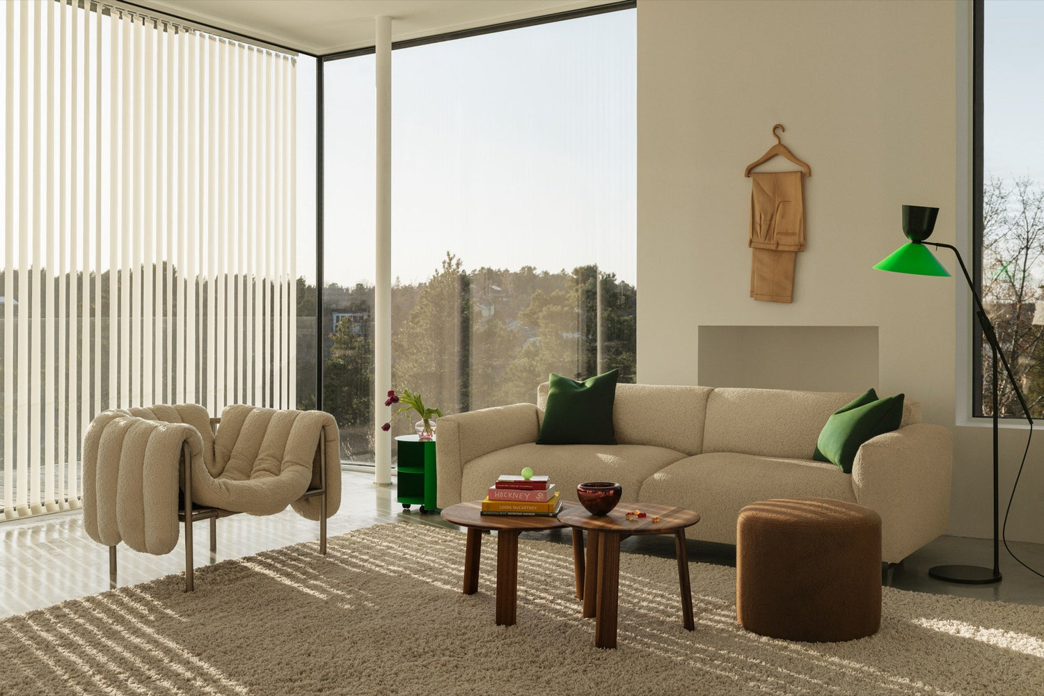 A living room scene featuring Puffy Lounge Chair in Eggshell / Stainless, Koti 3-seater sofa in Eggshell, Bon Pouf Round in Brown, Alphabeta Floor Lamp and Alle Coffee Tables set of 2 in Walnut.