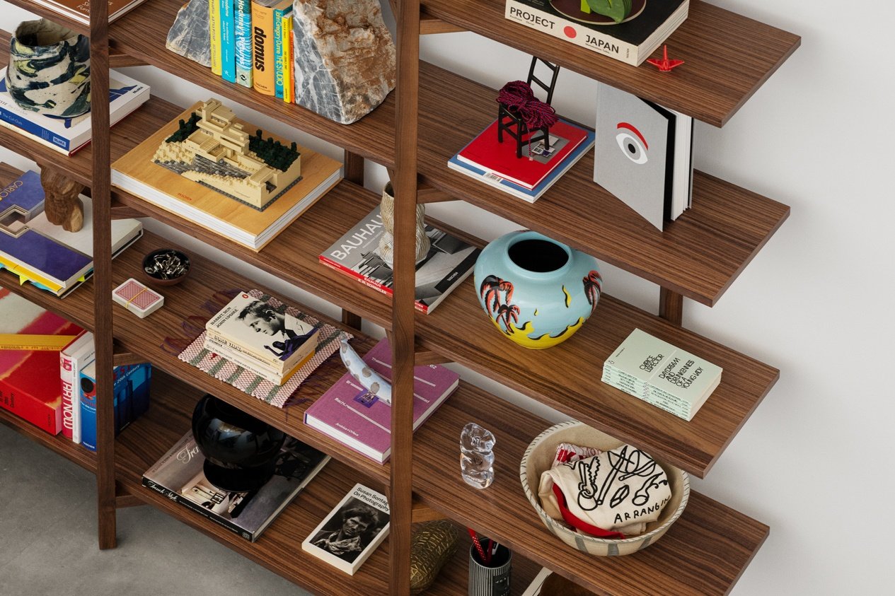 An aerial view of a Zig Zag High Shelf in the shade Walnut with books and other decorative objects placed in its shelves.